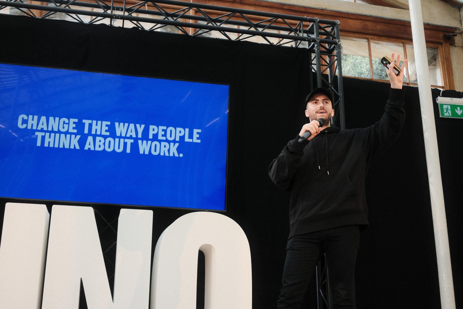 Man on stage with mic talking about changing the way people think about work